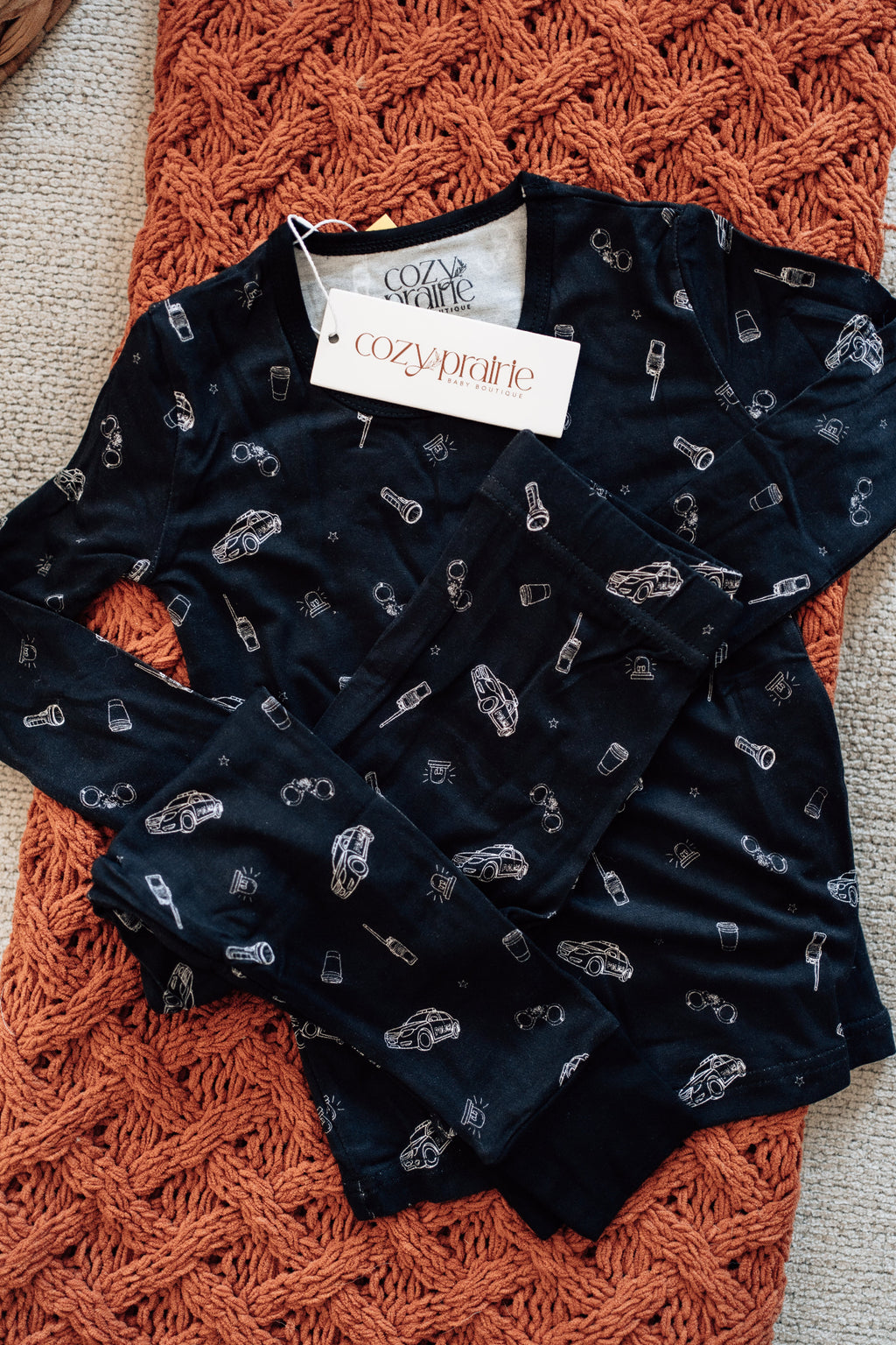 Black baby romper with car pattern on a textured orange surface, brand tag visible.