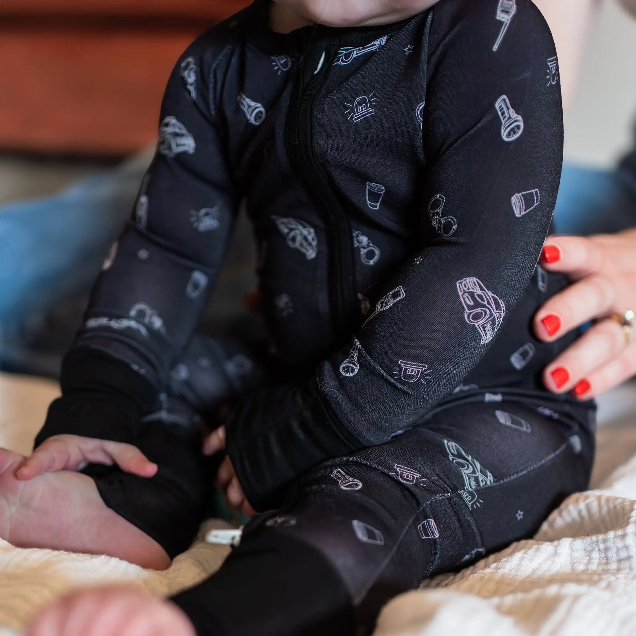 Baby wearing a black patterned onesie sitting on a blanket.