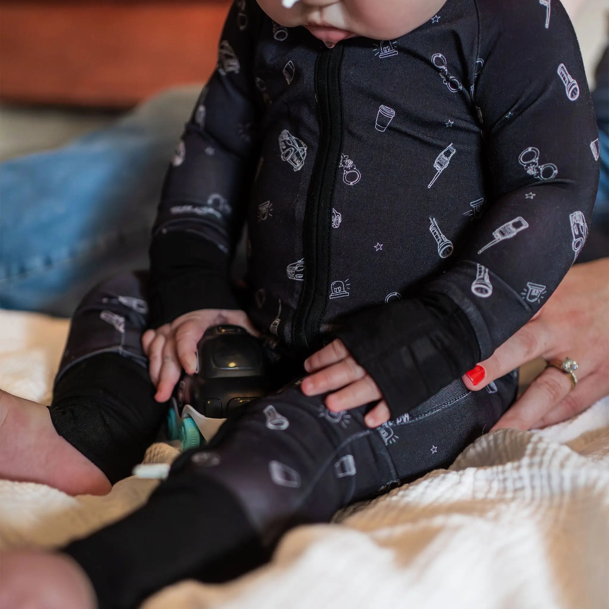 Child in a dark patterned onesie sitting on a couch with adult hands holding their feet.