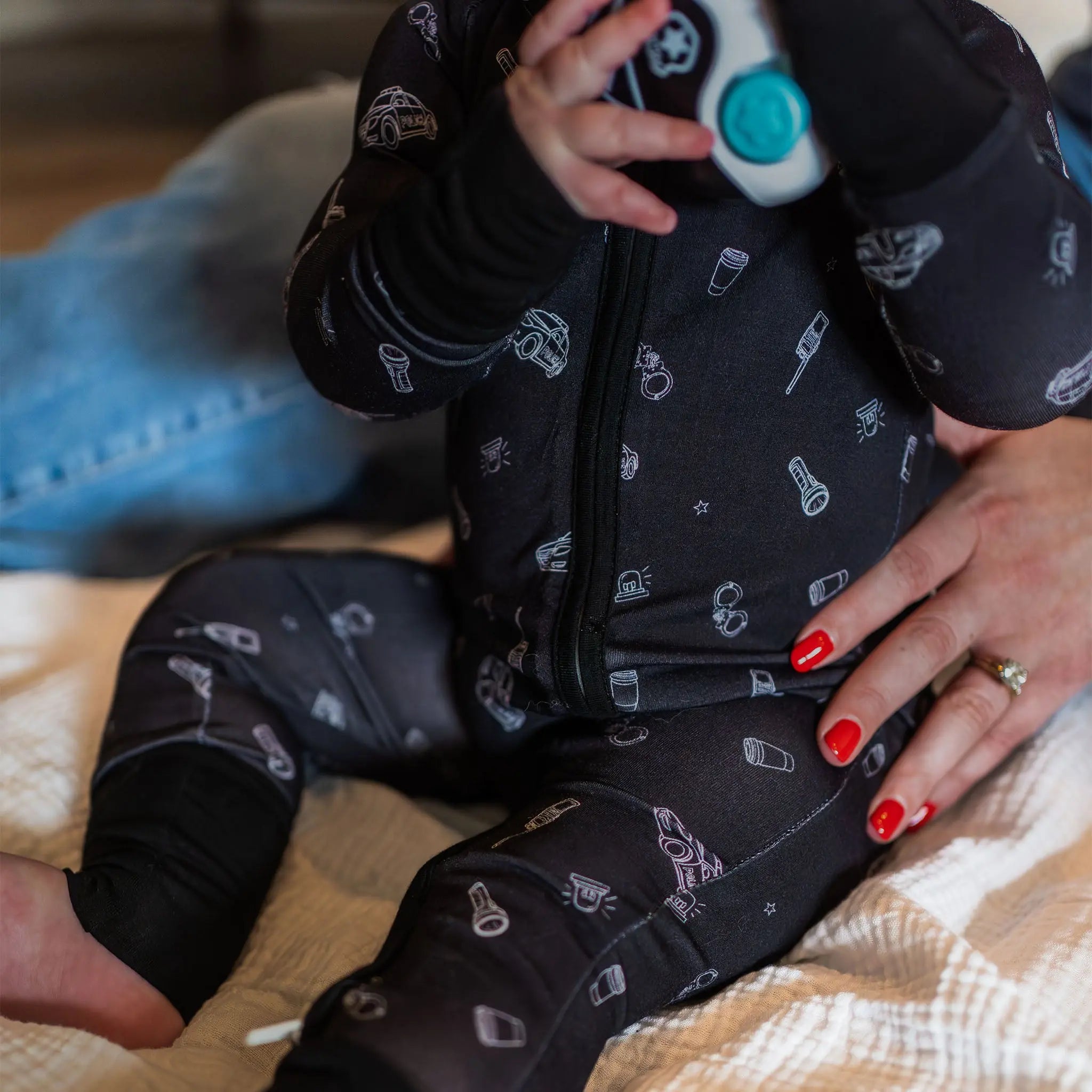 Baby in a black onesie with patterns, held by an adult on a wooden floor.