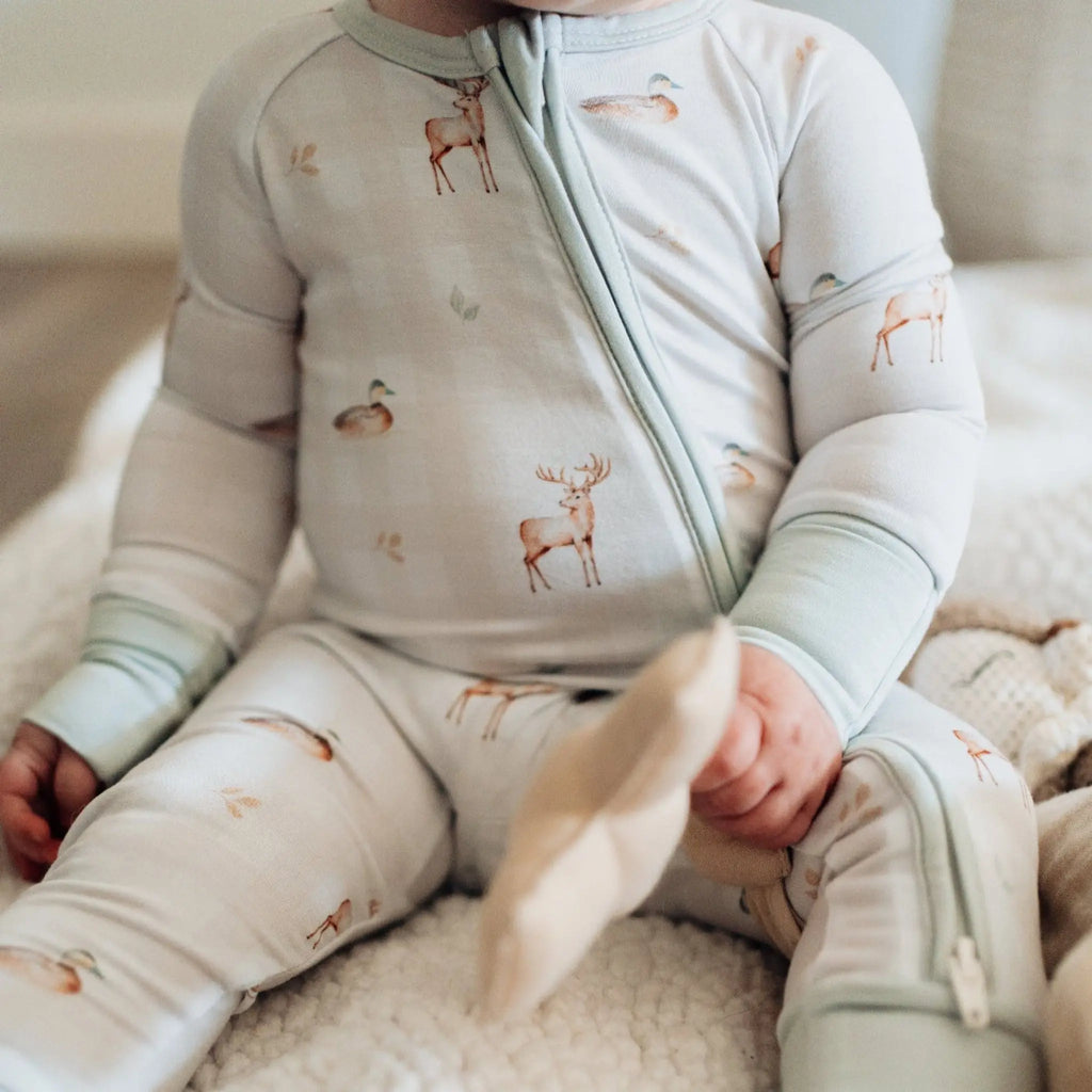 Baby wearing a light gray onesie with deer print sitting on a soft surface.