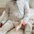 Baby wearing a light gray onesie with deer print sitting on a soft surface.