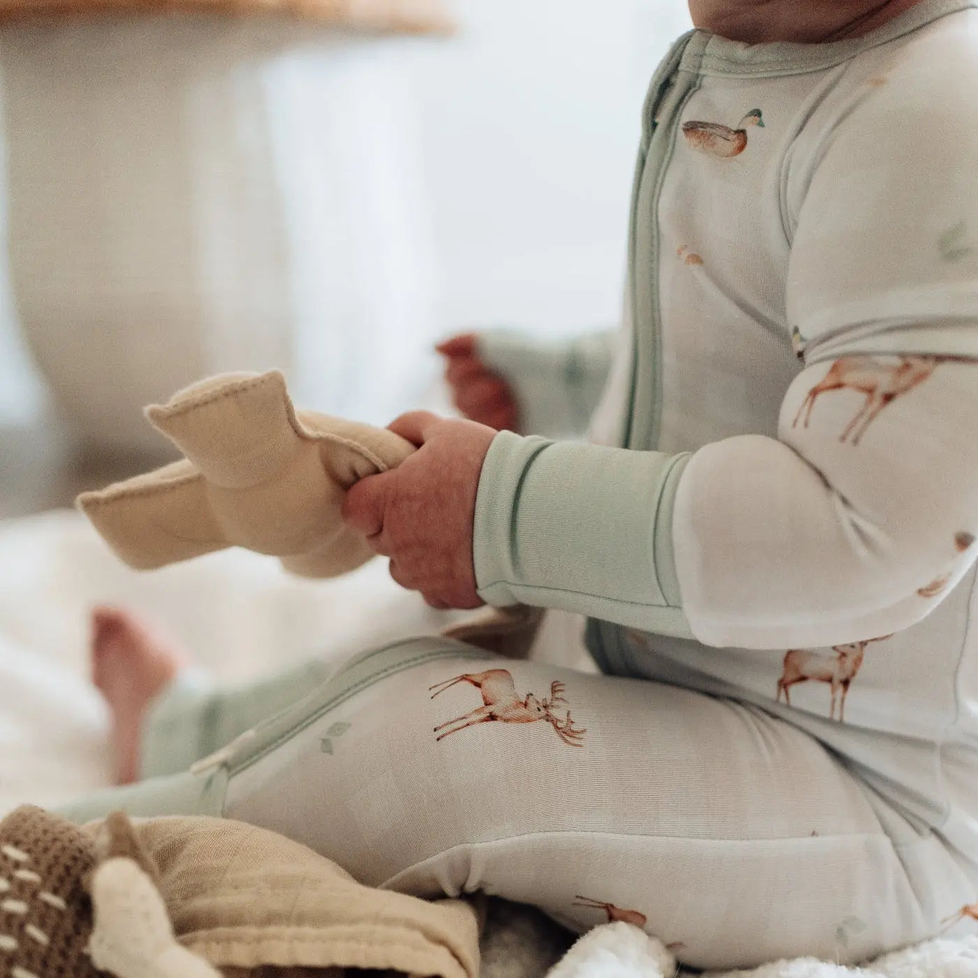 Child wearing a light green outfit with deer patterns, sitting on a white surface.