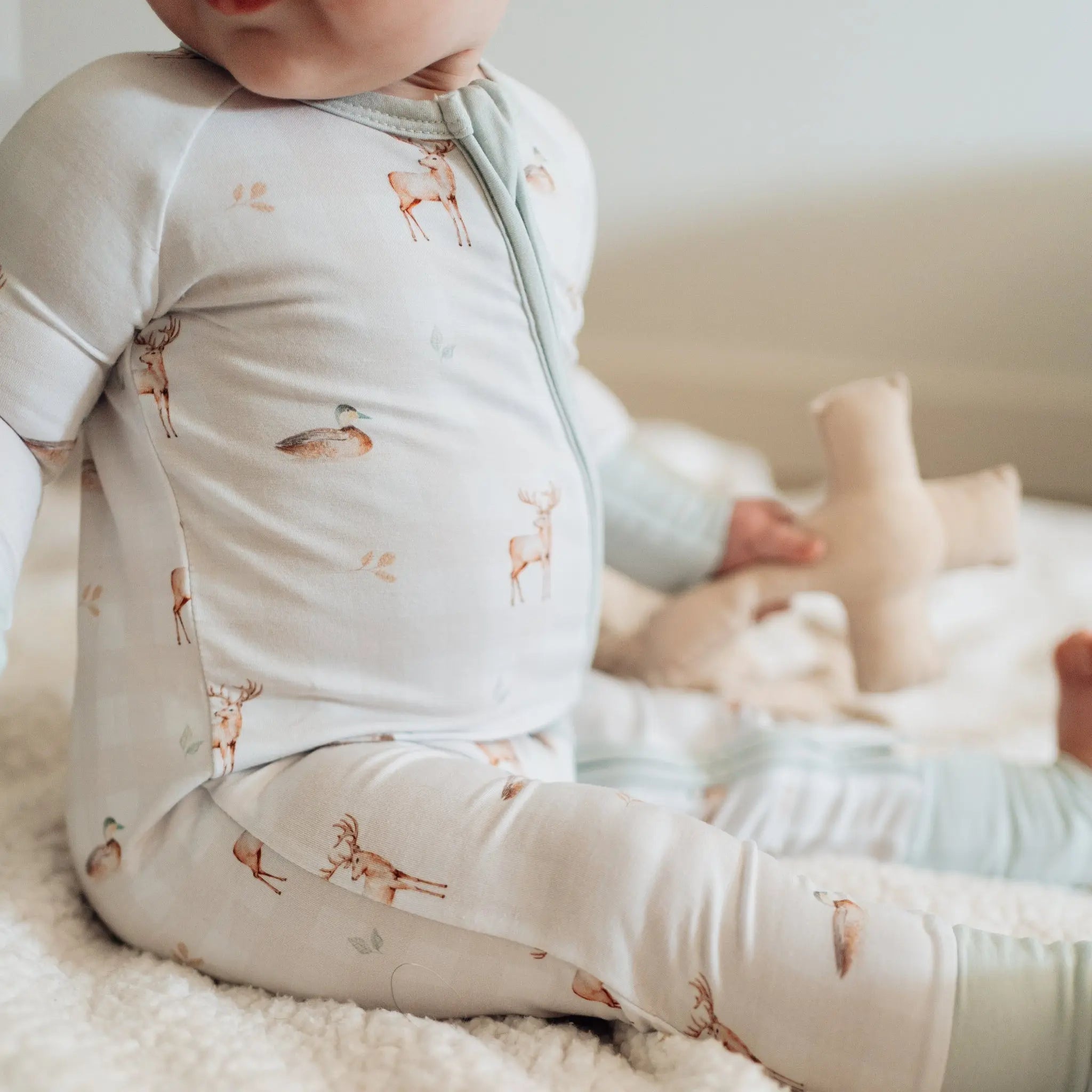 Baby wearing a light gray outfit with a pattern of small animals, sitting on a soft surface.