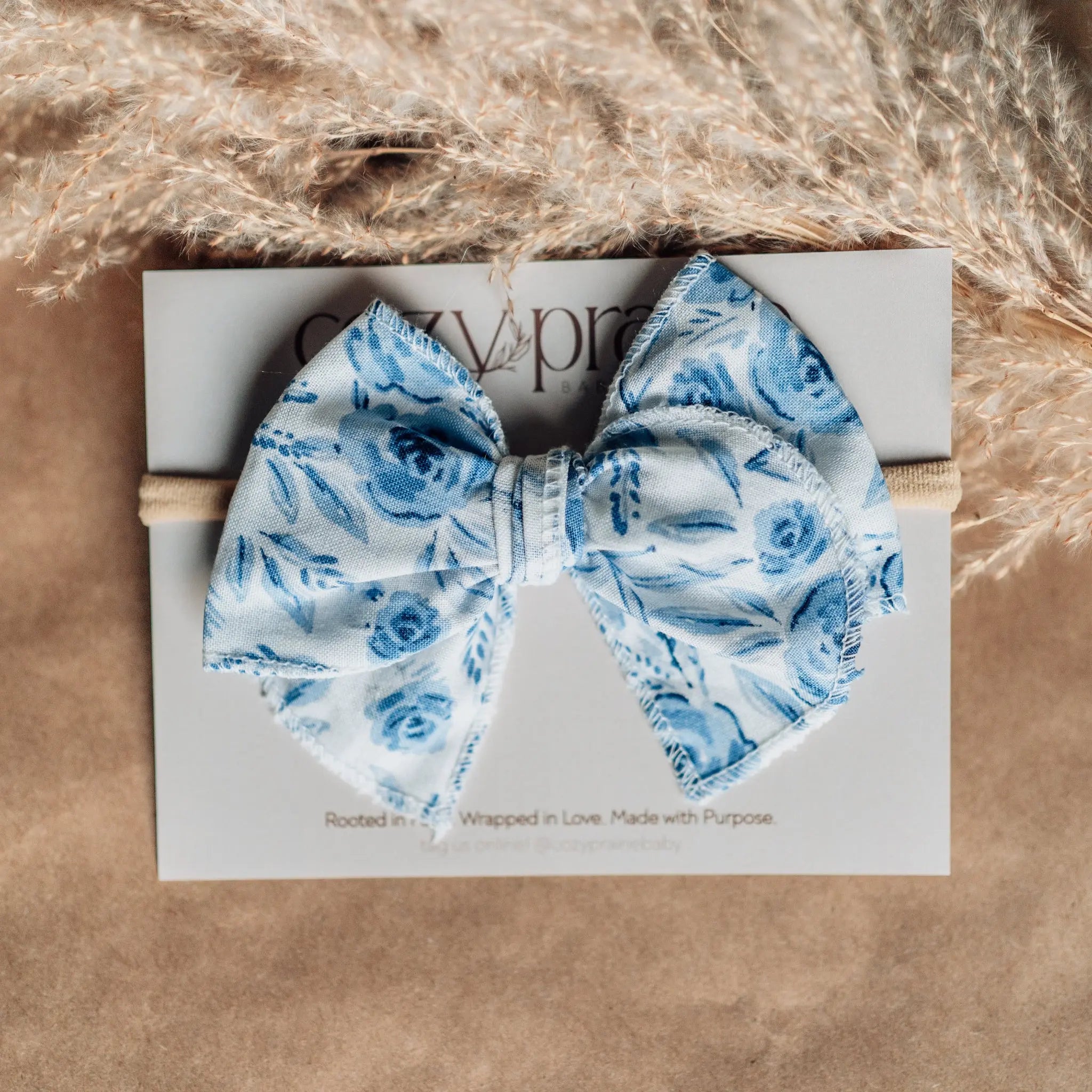 Blue floral bow tie on a branded box with dried pampas grass in the background