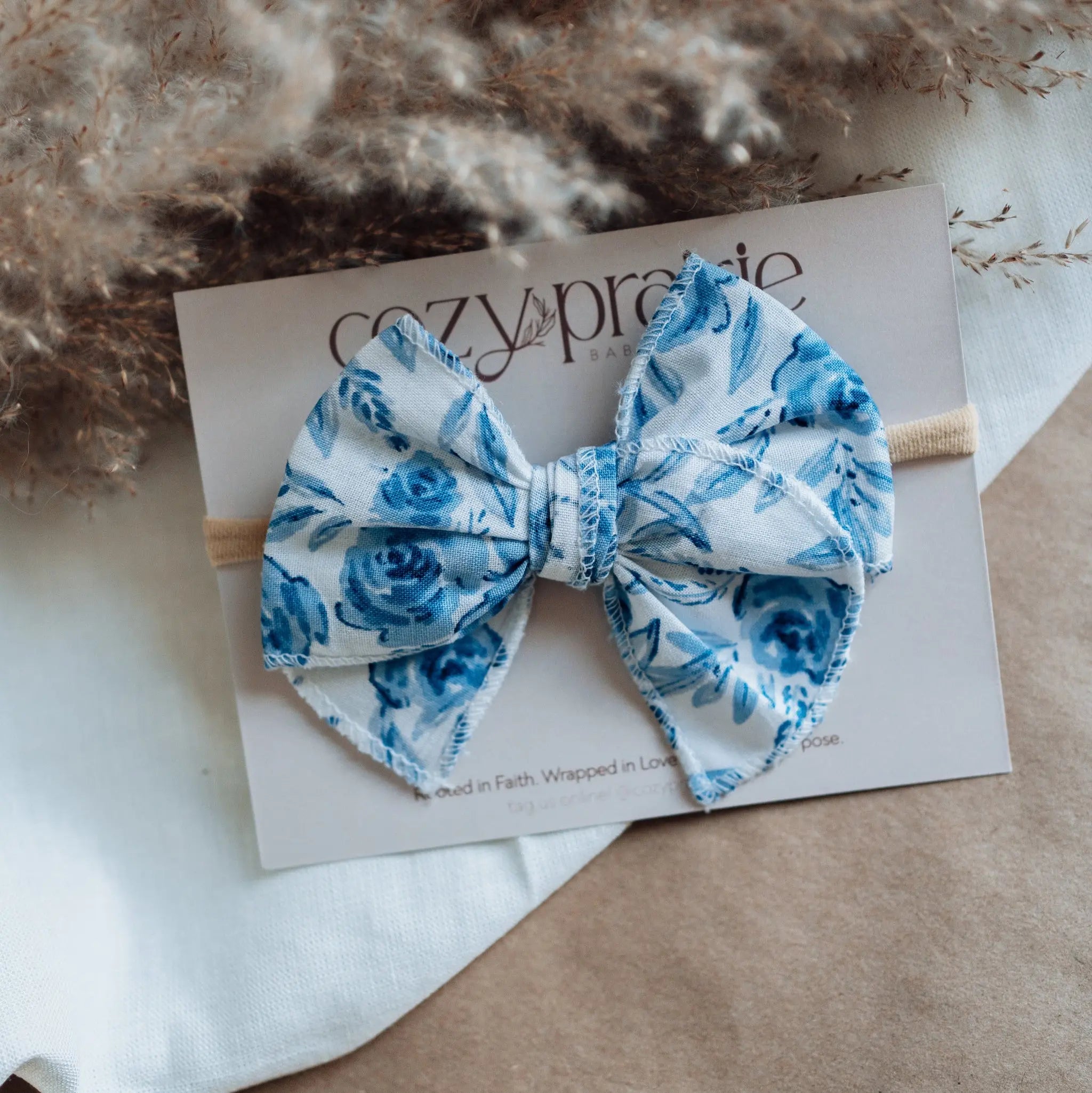 Blue floral bow on a white card with dried plants in the background