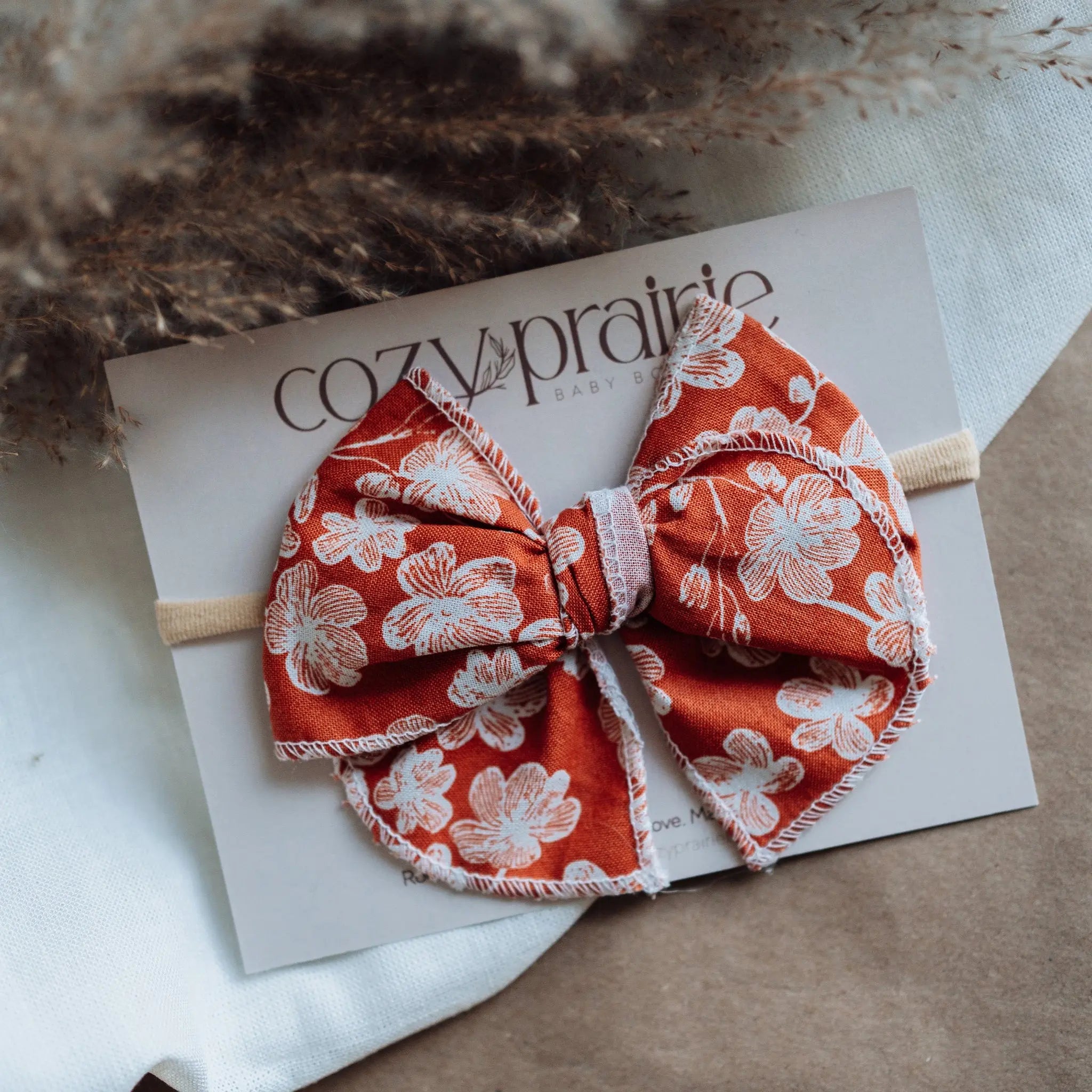 Red floral bow on a white card with 'Cozy Prairie' branding, placed on a textured surface.