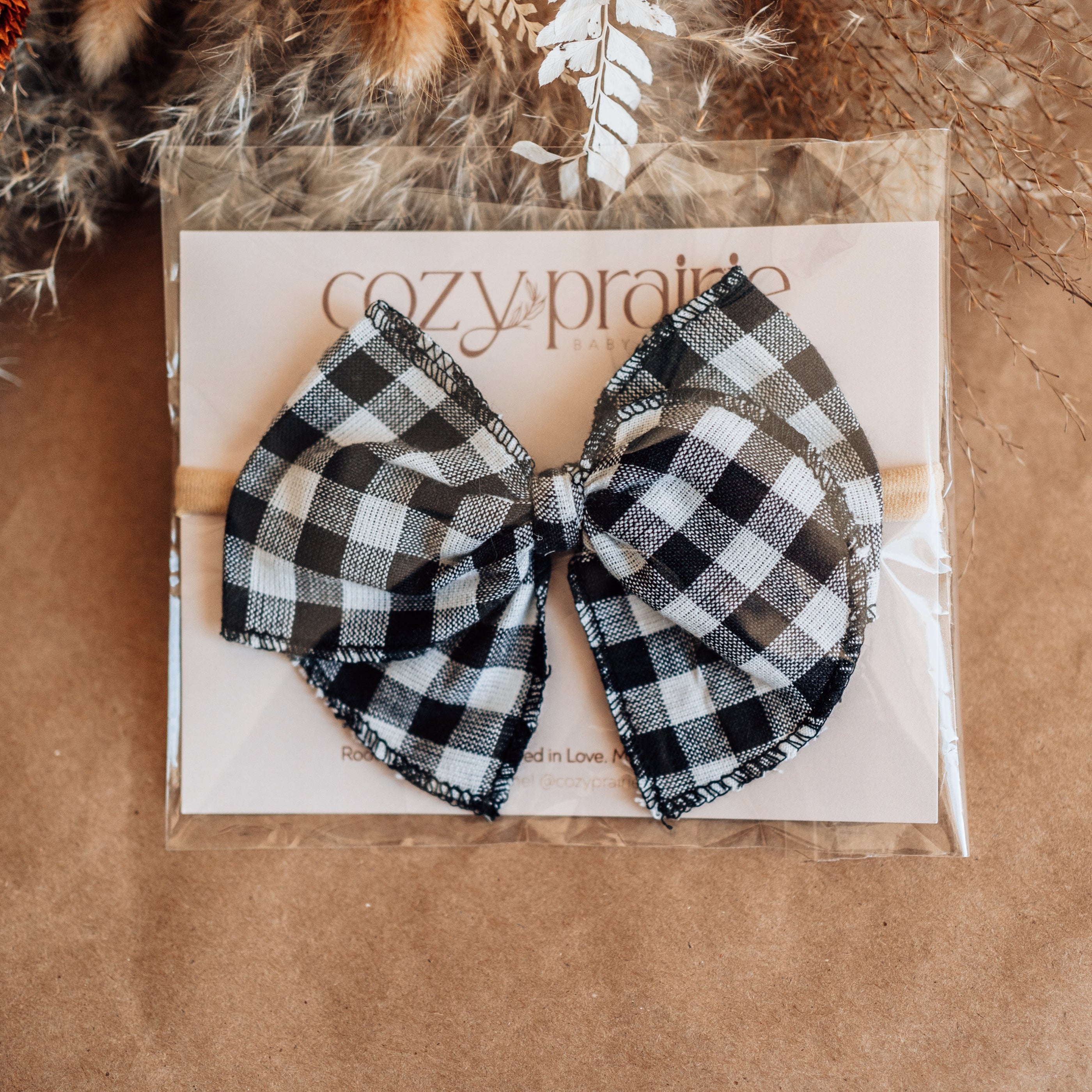 Black and white checkered bow on a Cozy Prairie branded card with dried plants in the background