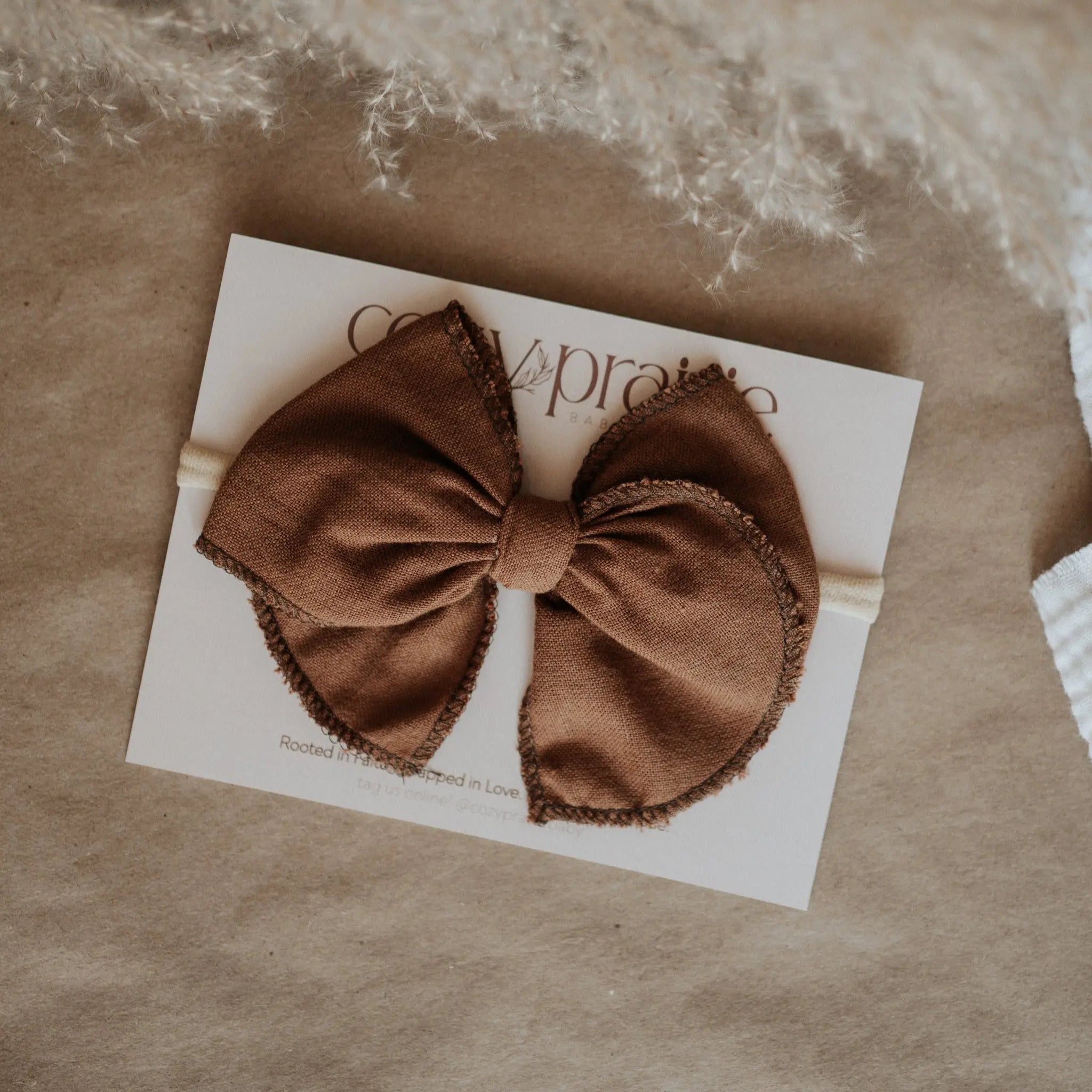 Brown bow hair accessory on a brand card with a textured background.