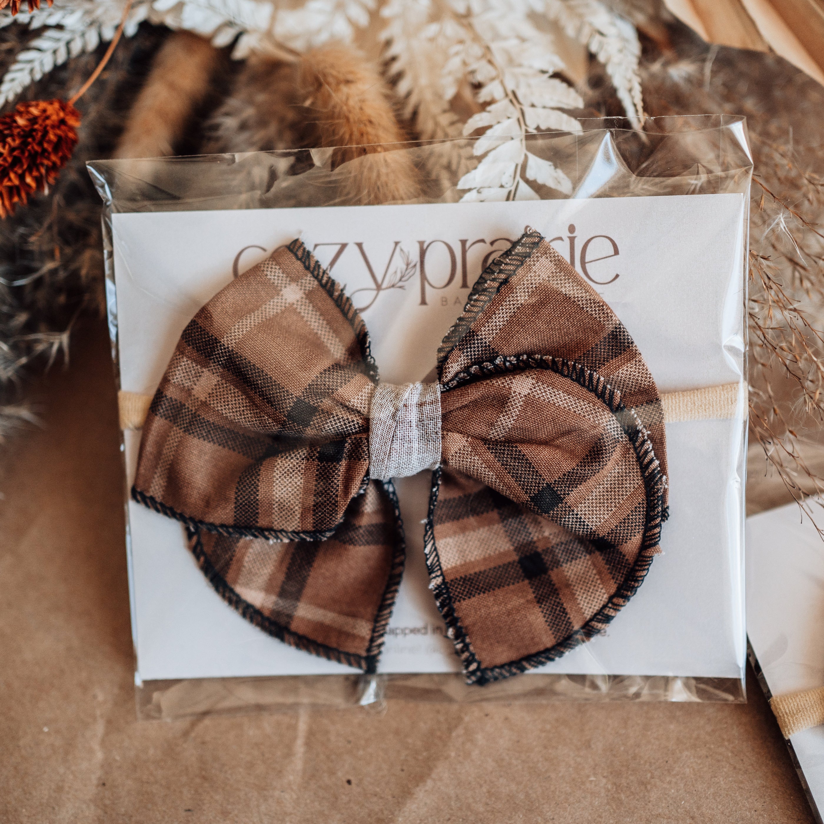 Plaid bow hair accessory on a branded card with decorative elements.