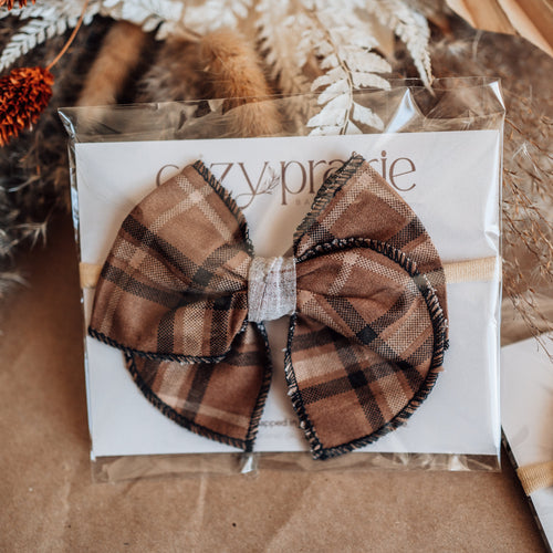 Plaid bow hair accessory on a branded card with decorative elements.