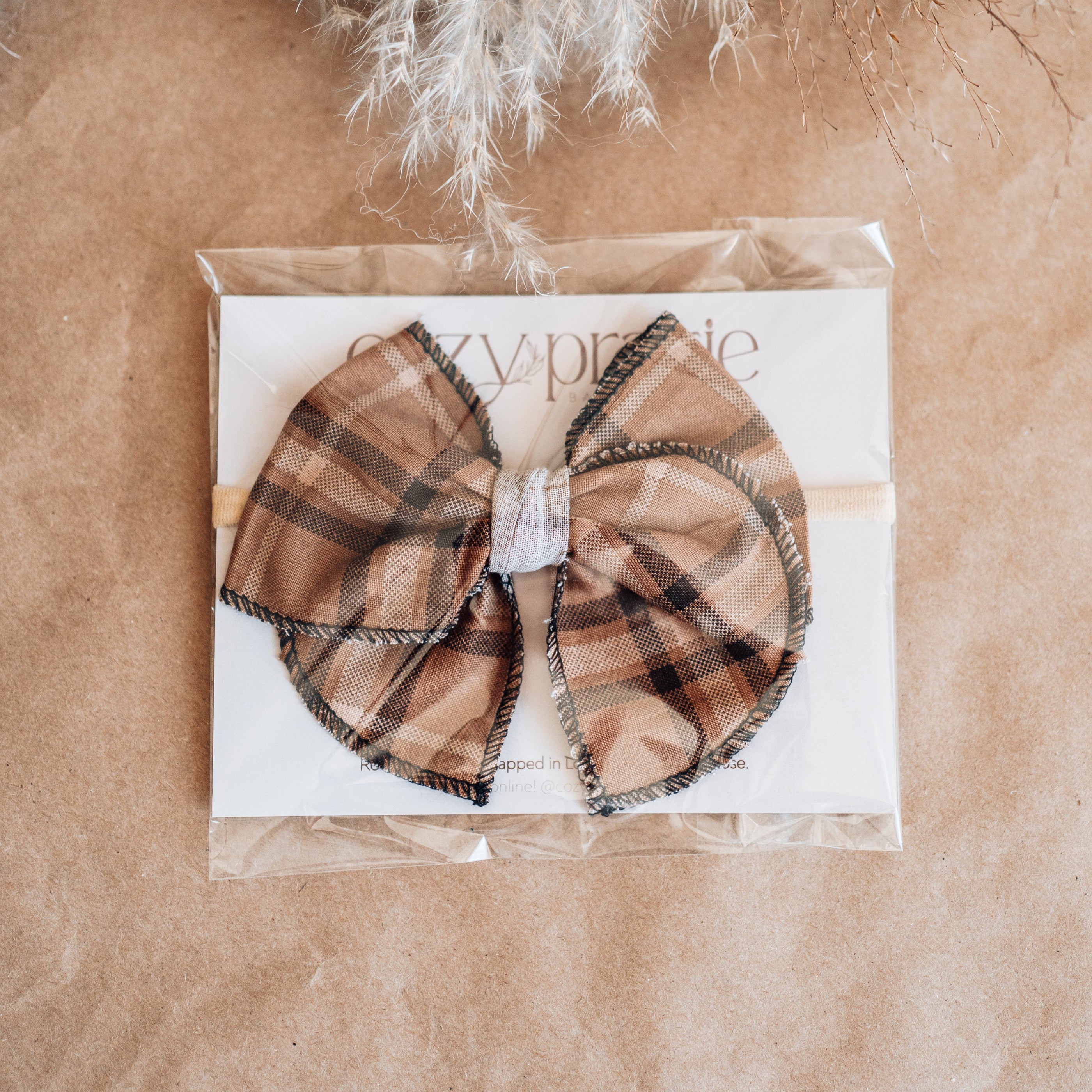 Plaid hair bow packaging on a brown surface with decorative elements