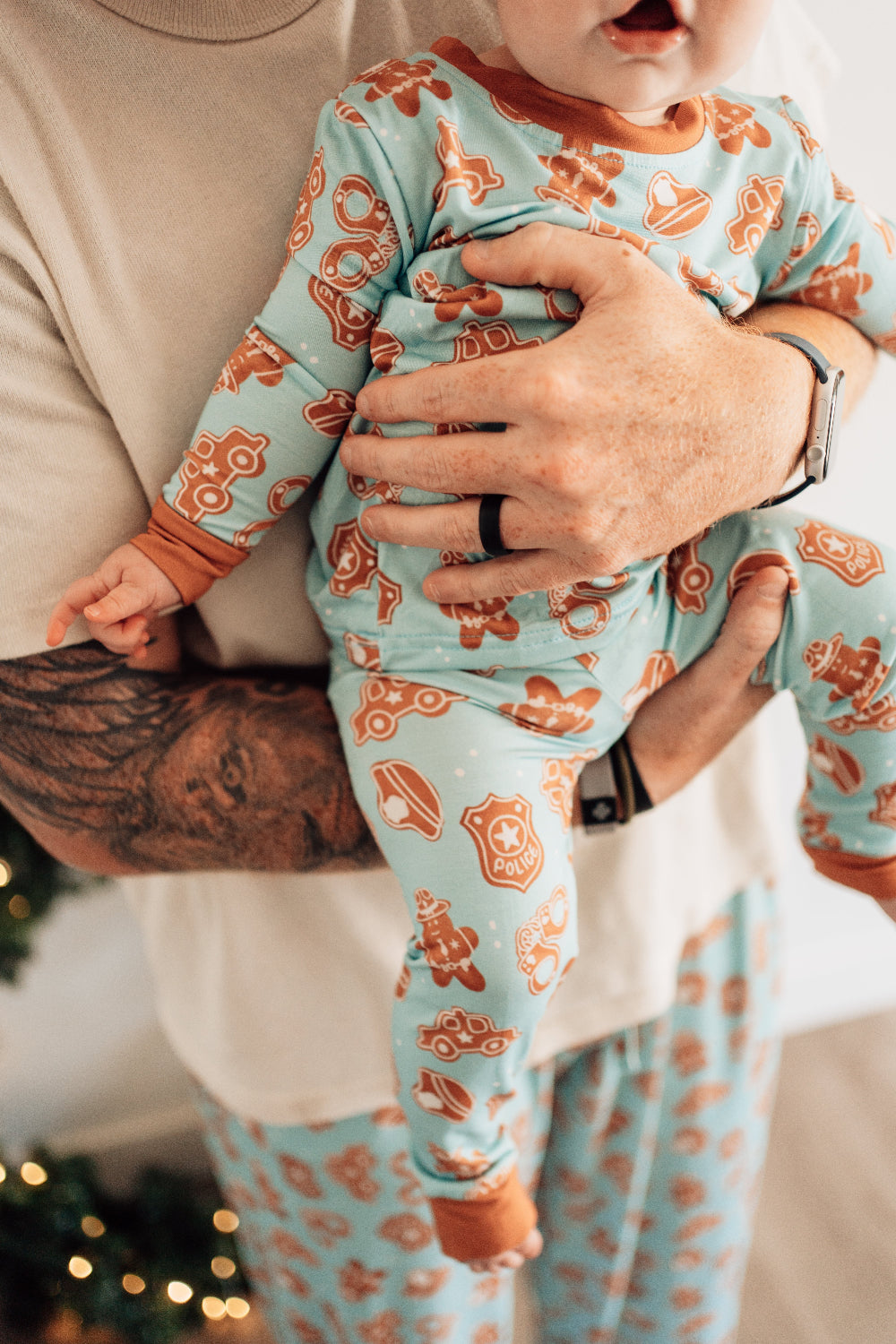 Person holding a child wearing matching pajamas with gingerbread men design.