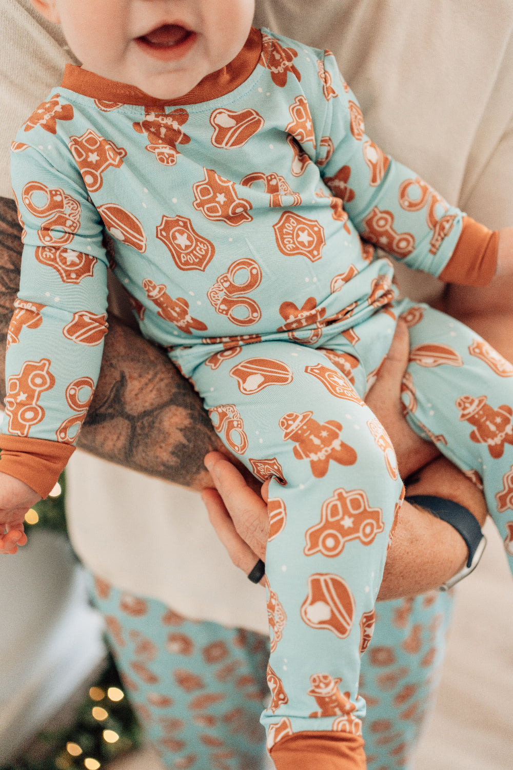 Baby wearing a light blue onesie with orange animal prints, held by an adult.