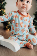 Baby wearing a blue and orange pajama set with Christmas tree in the background