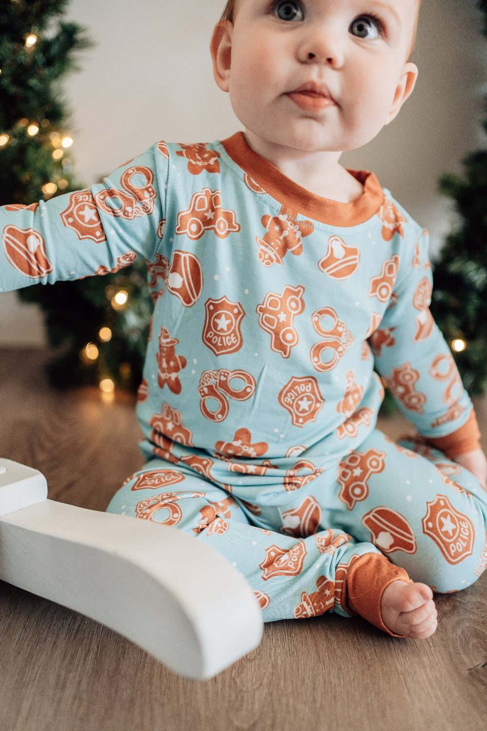 Baby wearing a blue and orange pajama set with Christmas tree in the background
