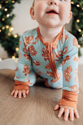 Baby wearing a blue and orange pajama set with Christmas tree in the background