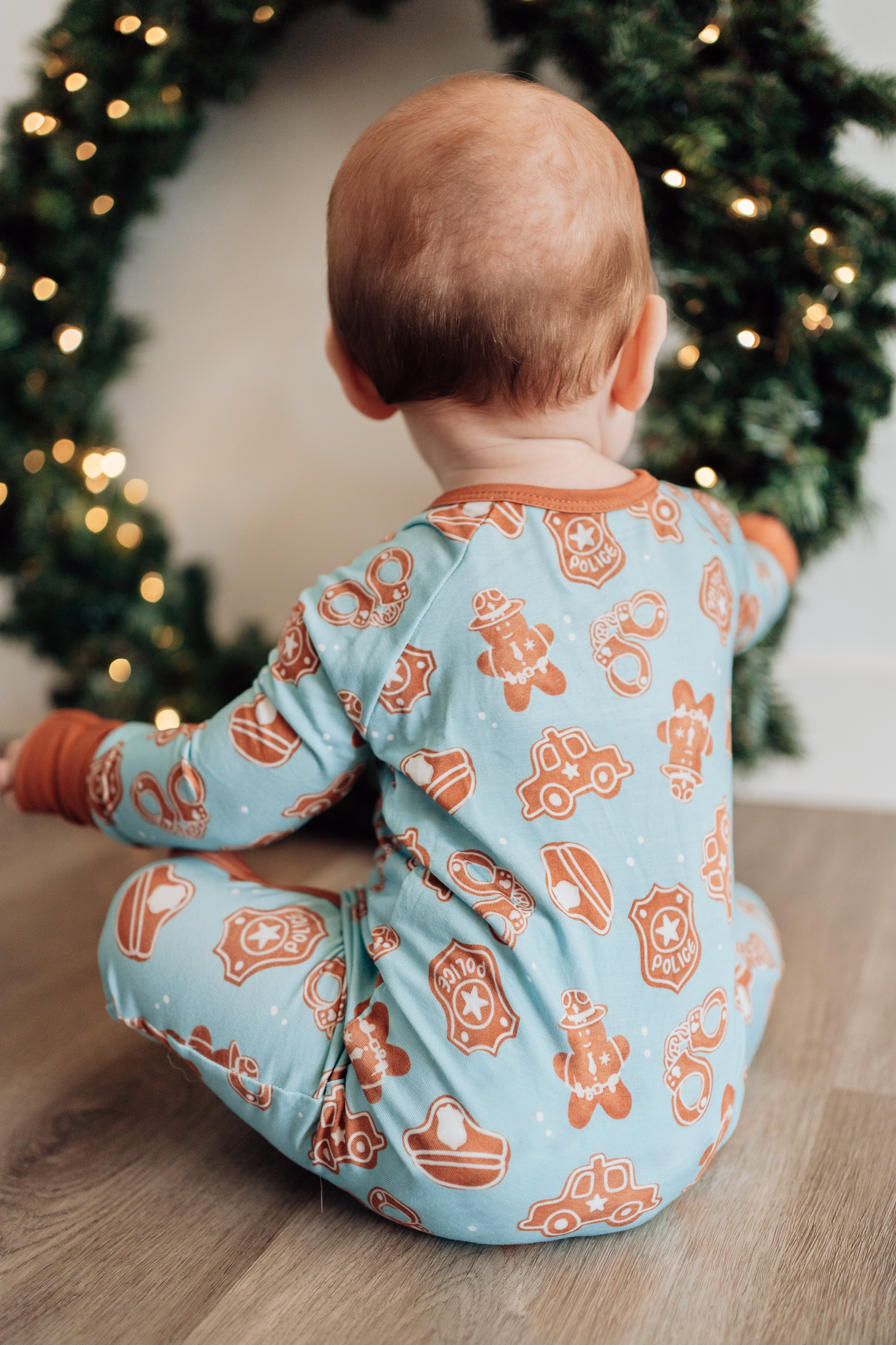 Baby wearing a blue and orange pajama set with Christmas tree in the background