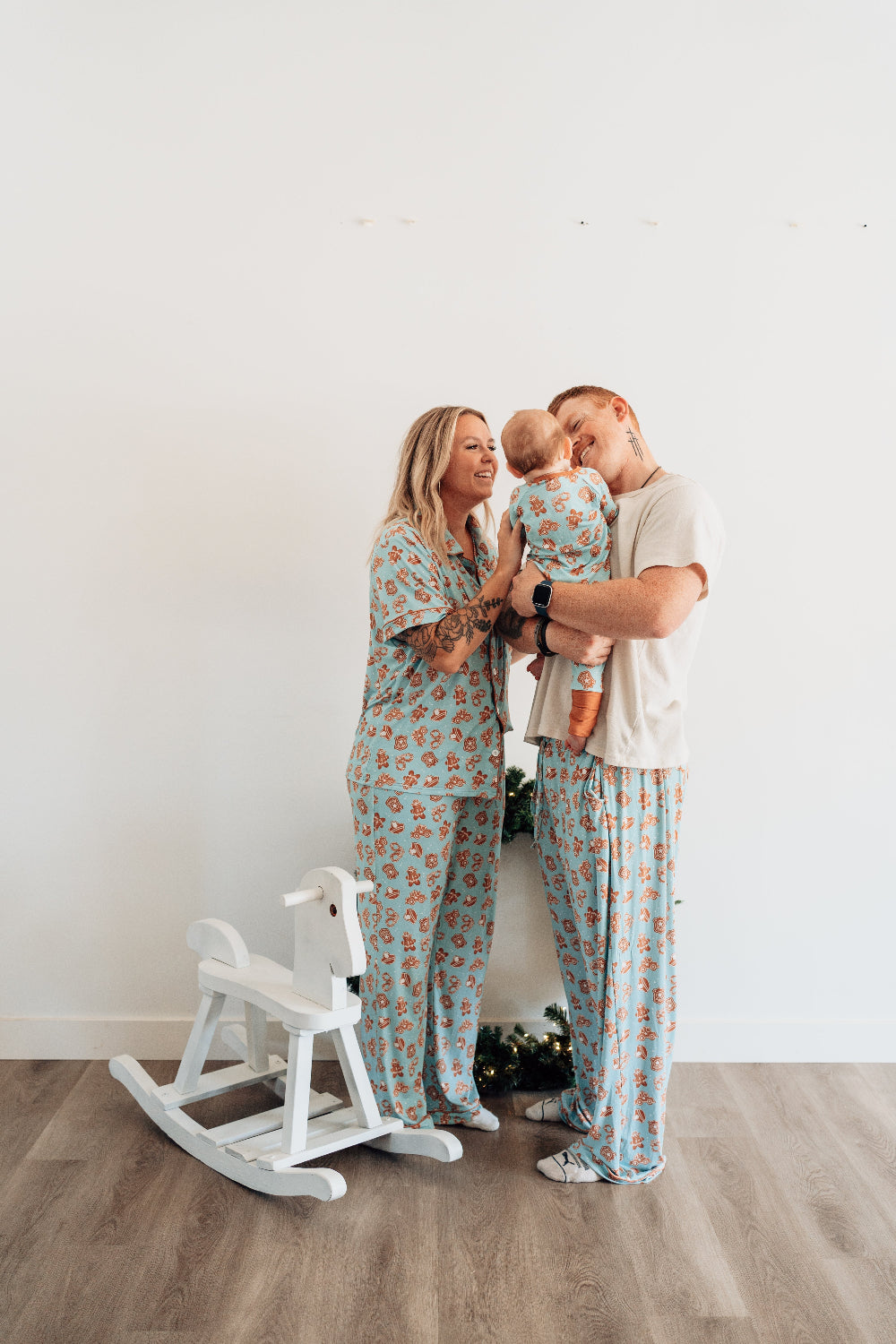 Family of three wearing matching pajama sets in a room with a white wall and wooden floor.