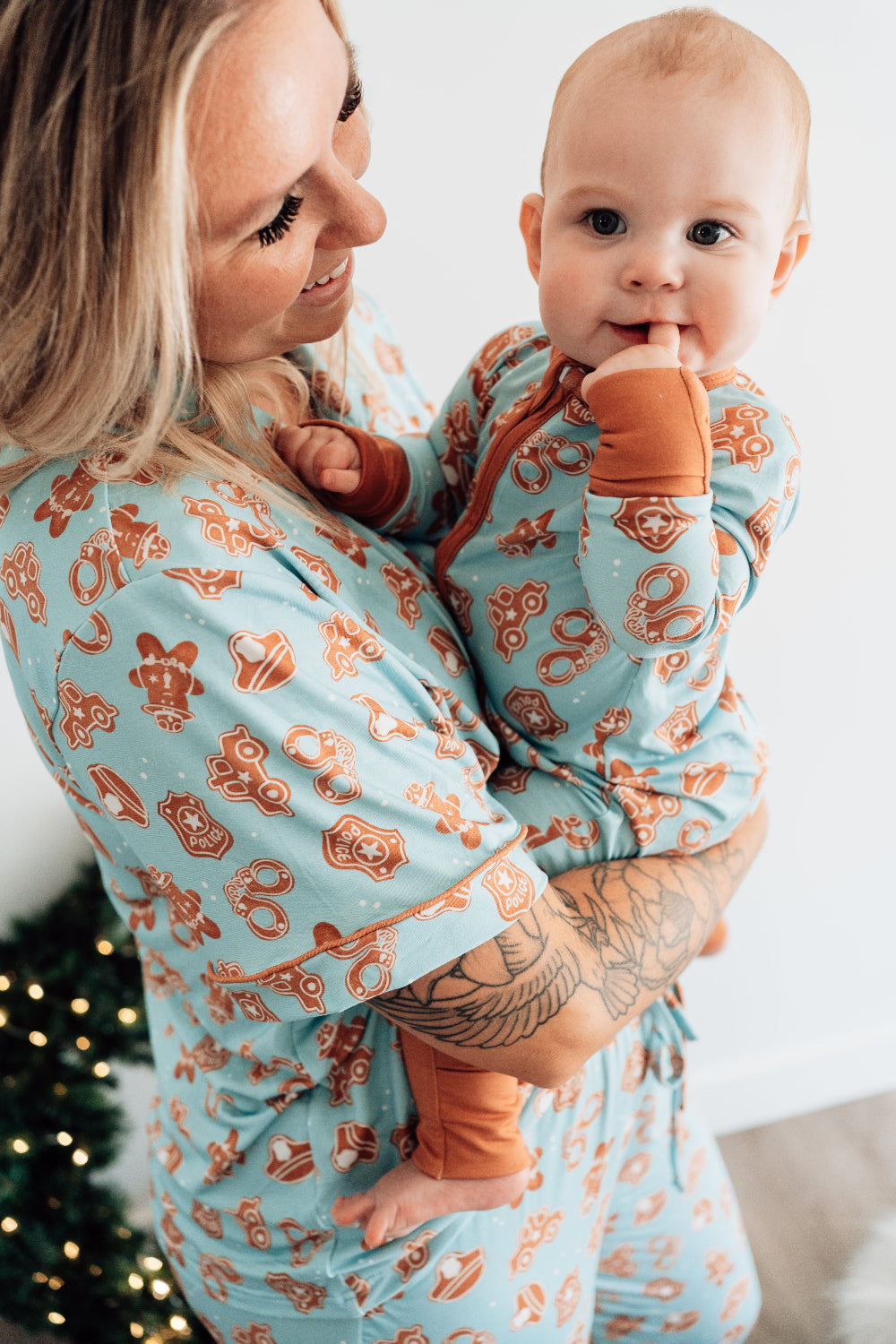 Woman holding a baby wrapped in a matching blue and orange patterned blanket with a Christmas tree in the background.