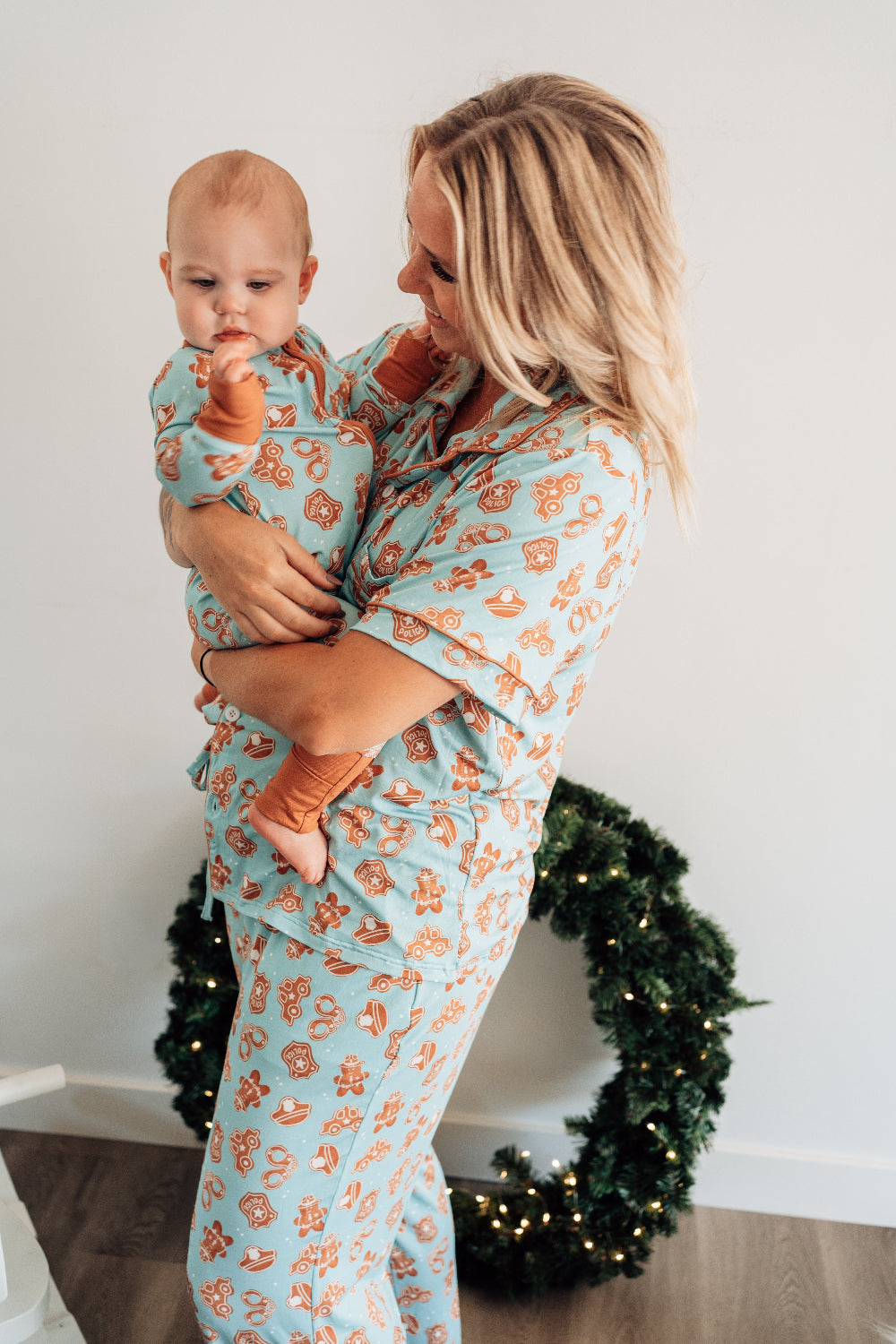 Woman holding a baby in matching pajamas with a Christmas wreath in the background
