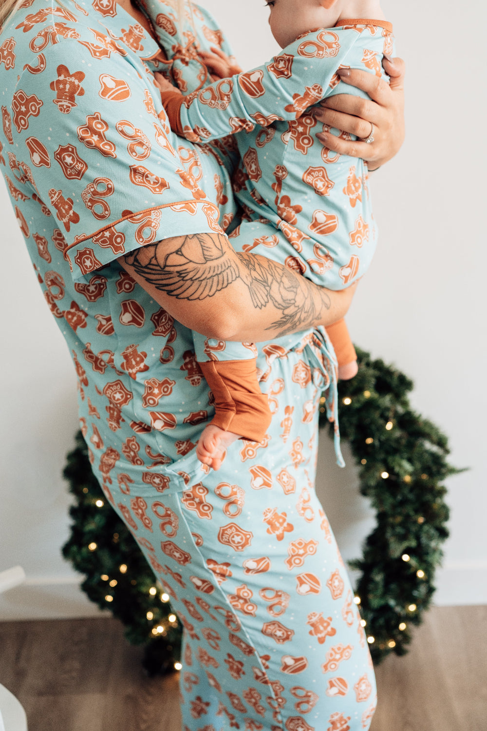 Person wearing matching pajama sets with a baby, standing in front of a decorated Christmas wreath.