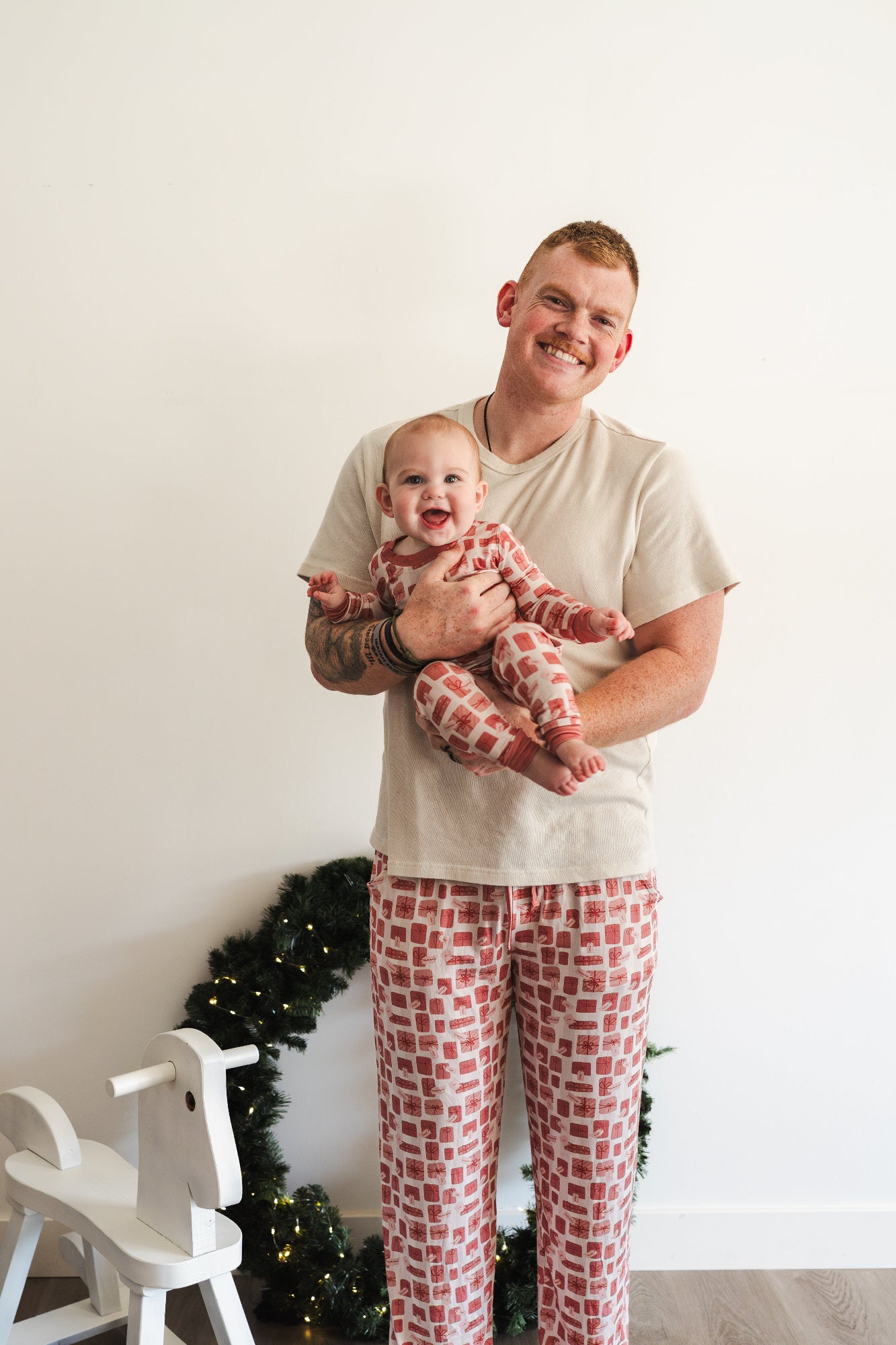 Man and baby in matching pajamas standing in front of a Christmas tree.