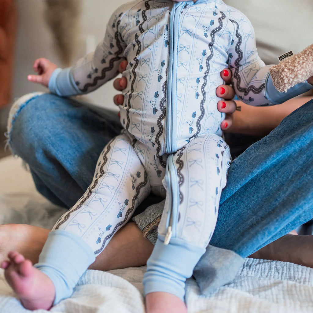 Baby in light blue outfit with patterns sitting on a lap.