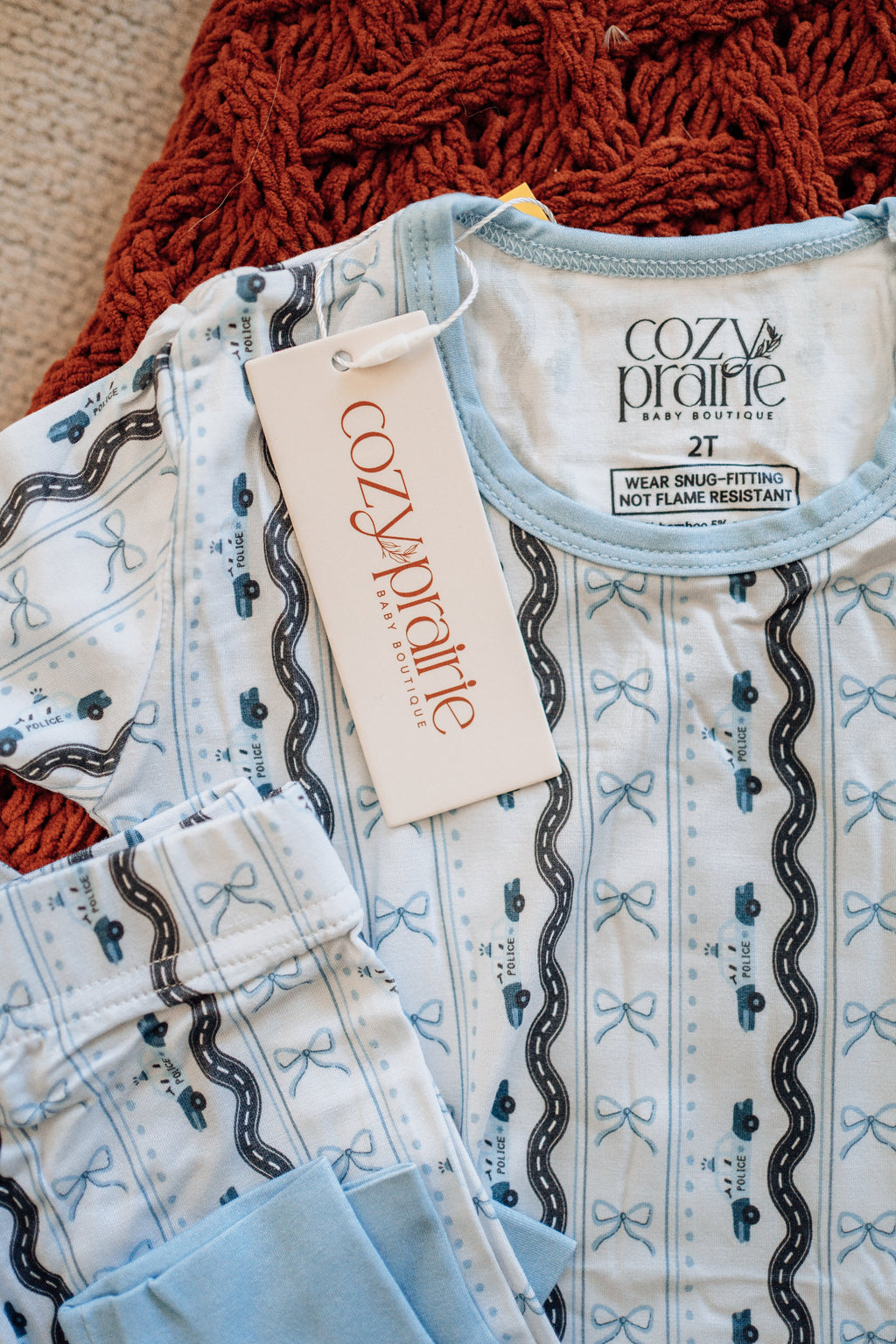 Baby onesie with bow pattern and 'Cozy Prairie' tag on a textured surface