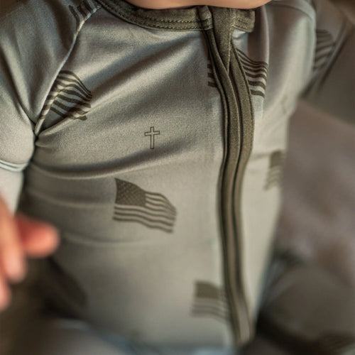 Close-up of a baby wearing a green long-sleeve zip romper with a cross and American flag design.