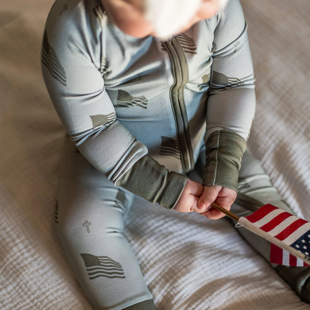 Child wearing a onesie with flag designs, holding an American flag.