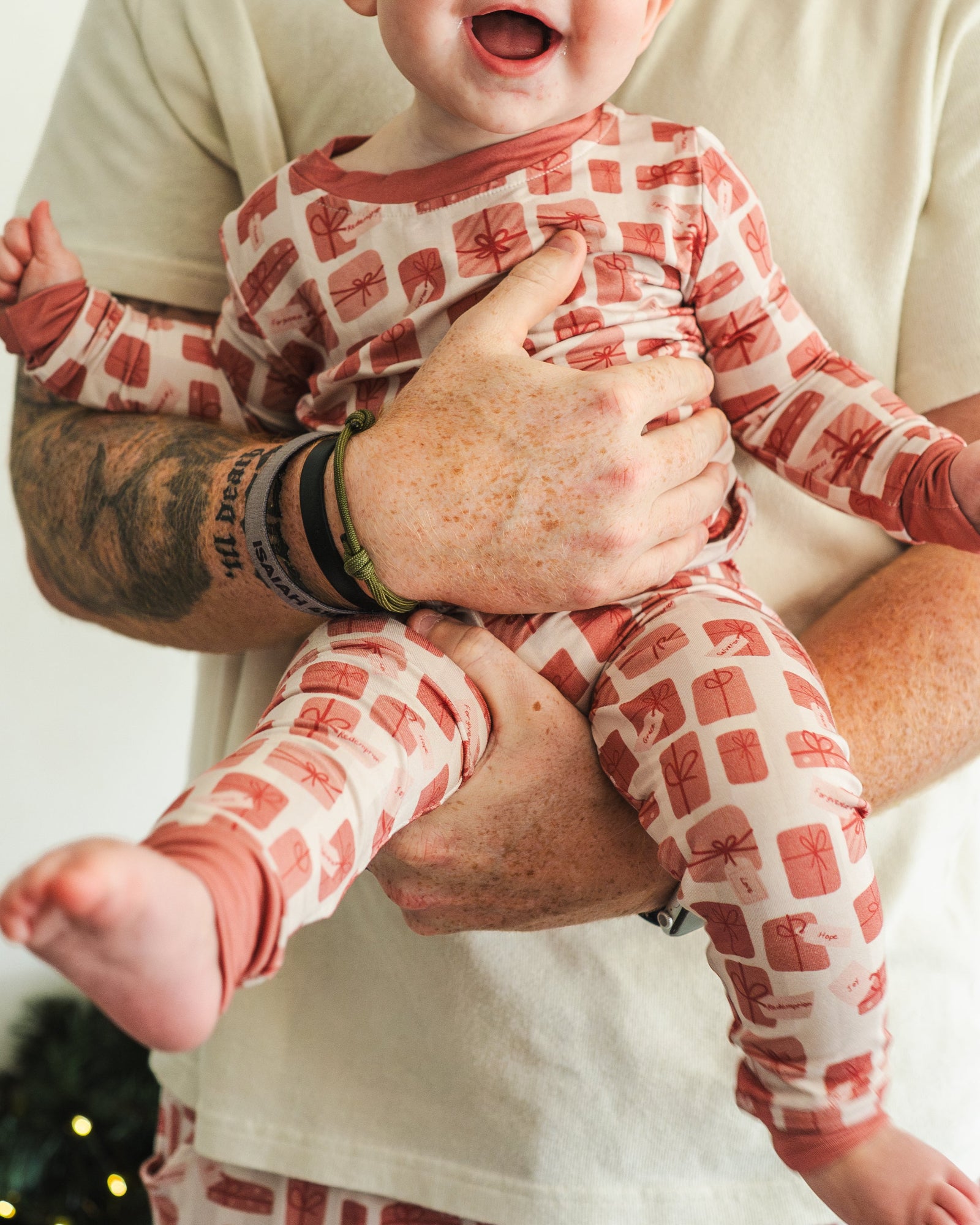 Person holding a baby wearing red and white checkered pajamas against a plain background