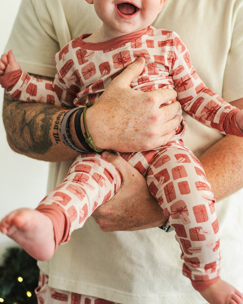 Person holding a baby wearing red and white checkered pajamas against a plain background