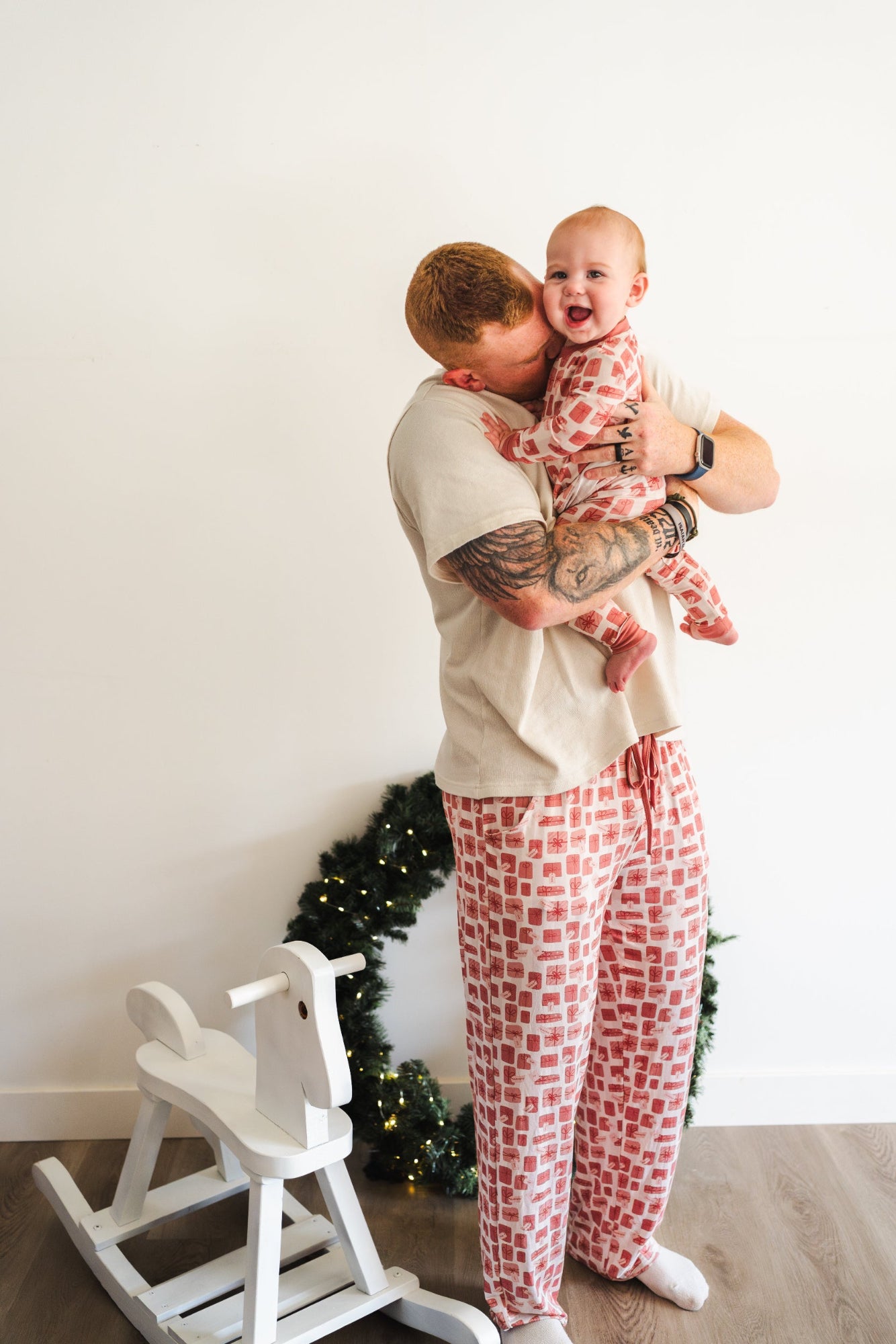 Man and child in matching pajamas standing in front of a Christmas tree.