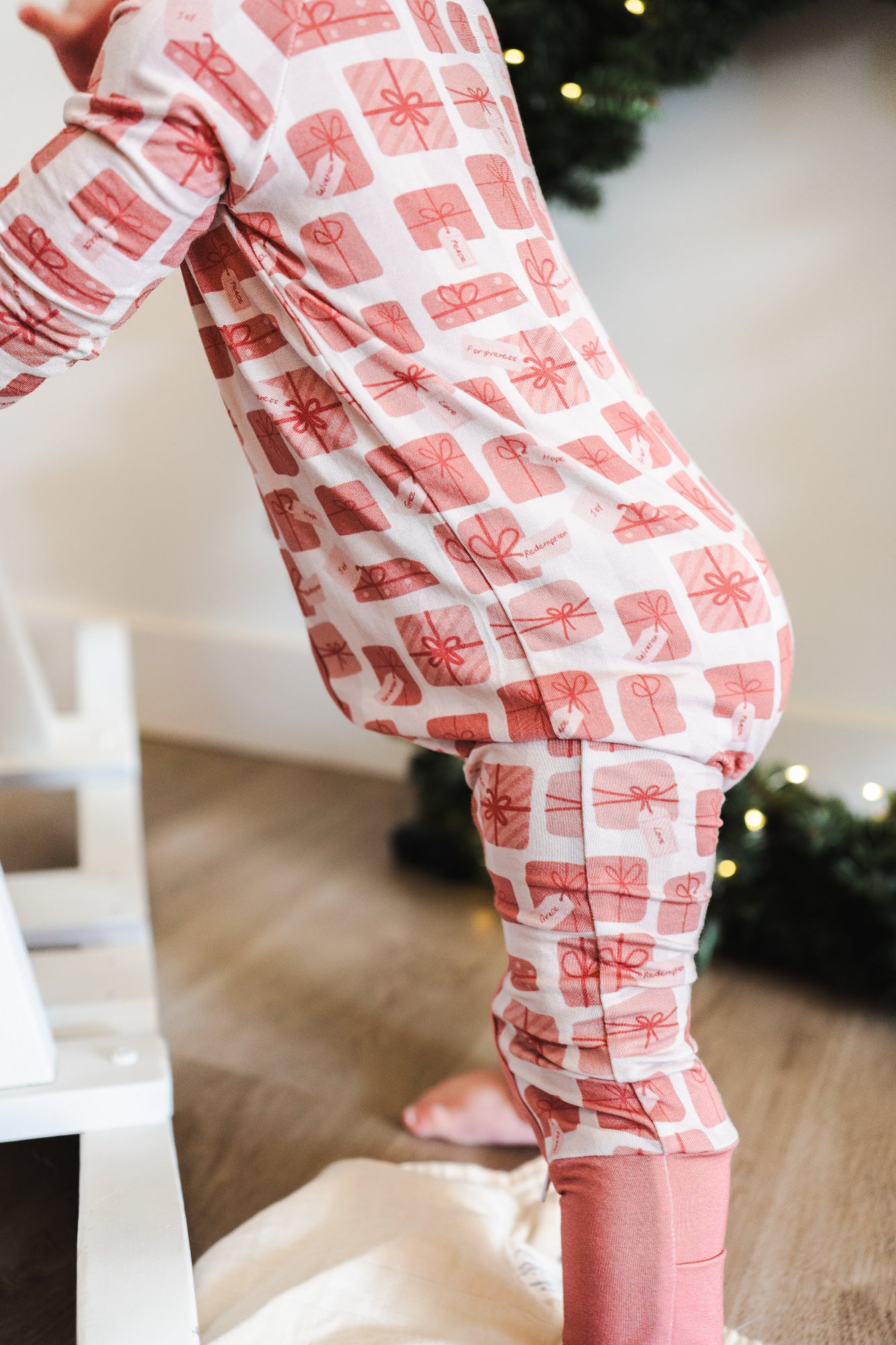 Child wearing red and white checkered pajama pants with a blurred Christmas tree in the background.