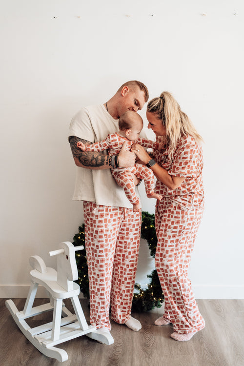 Family of three wearing matching pajamas in a home setting with a Christmas tree.
