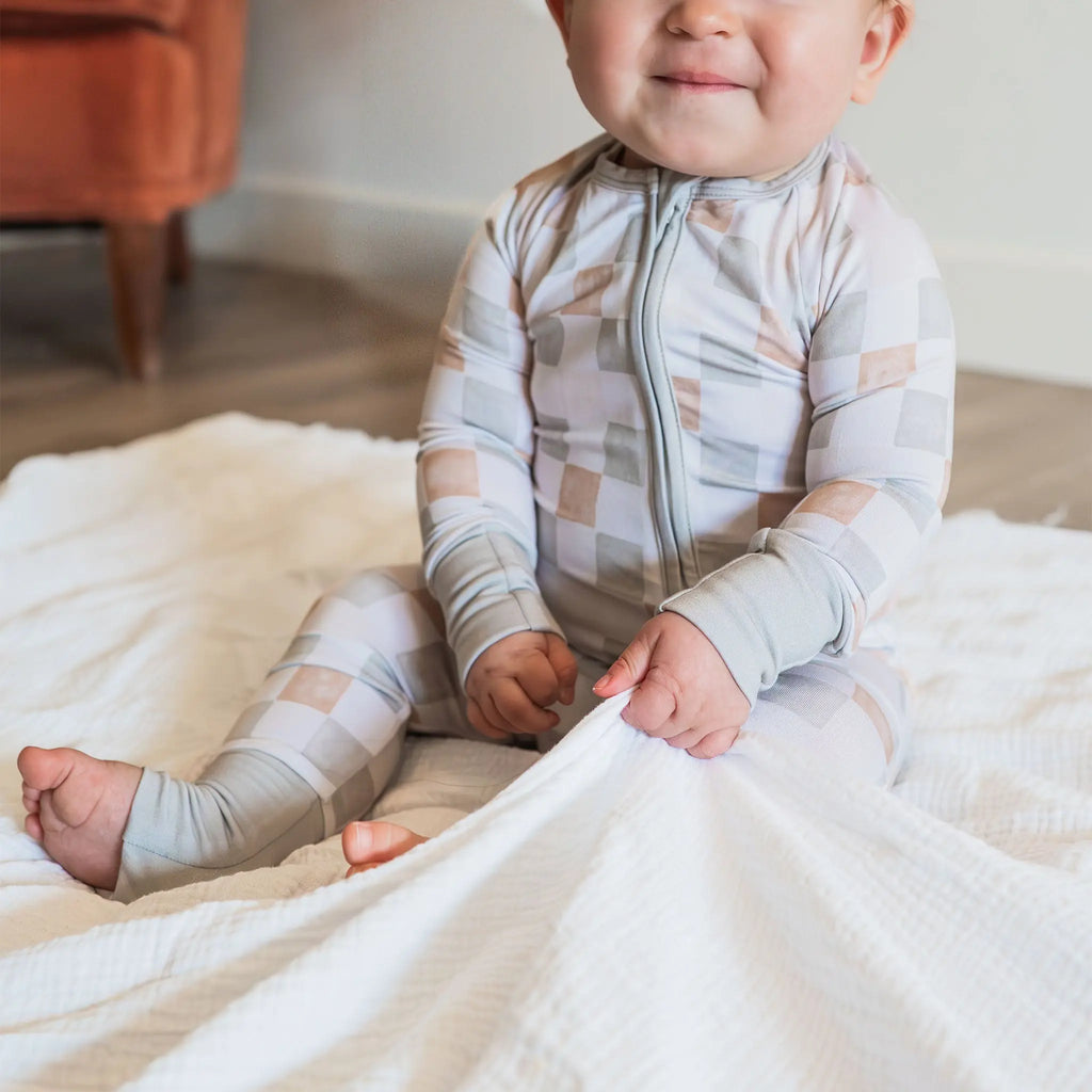 Baby in a checkered onesie sitting on a bed