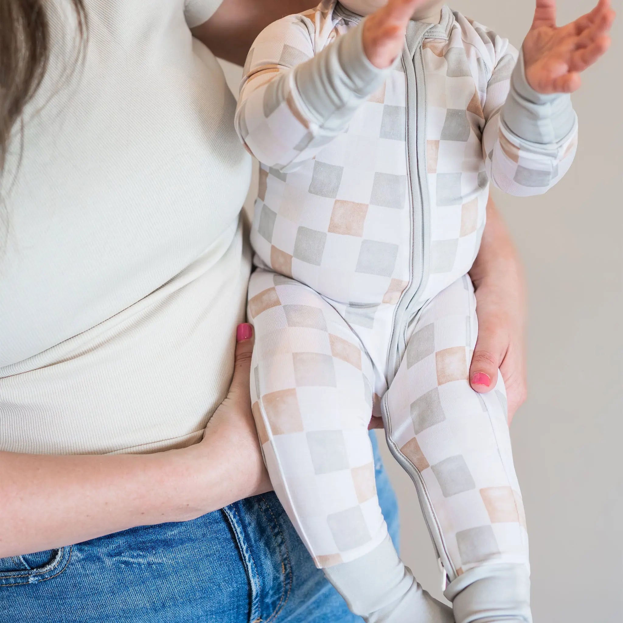 Person holding a baby wearing a patterned onesie against a neutral background
