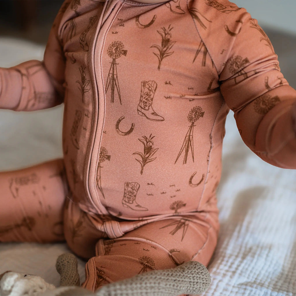 Baby in a rust onesie with cowboy boot and windmill pattern on a neutral background