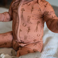 Baby in a rust onesie with cowboy boot and windmill pattern on a neutral background