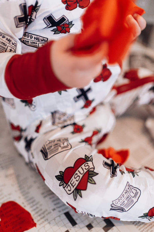 Close-up of a child's arm with red and white sleeve featuring 'Jesus' design, wearing a patterned outfit.