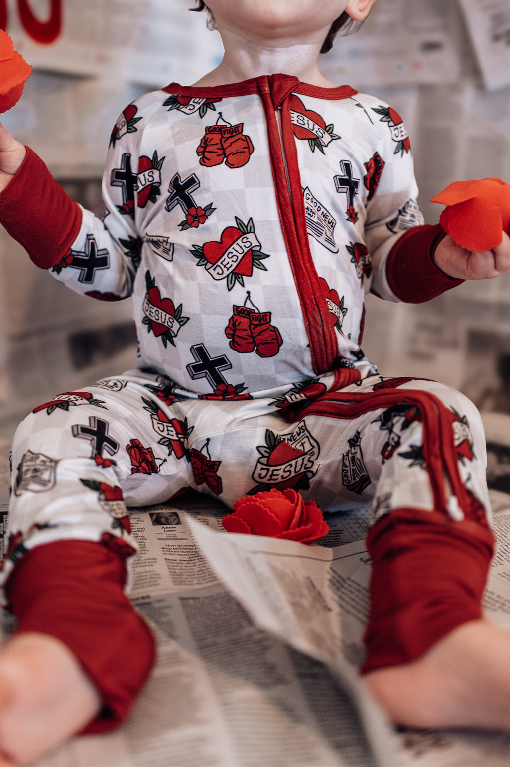 Child wearing a red and white pajama set with heart designs on a newspaper background