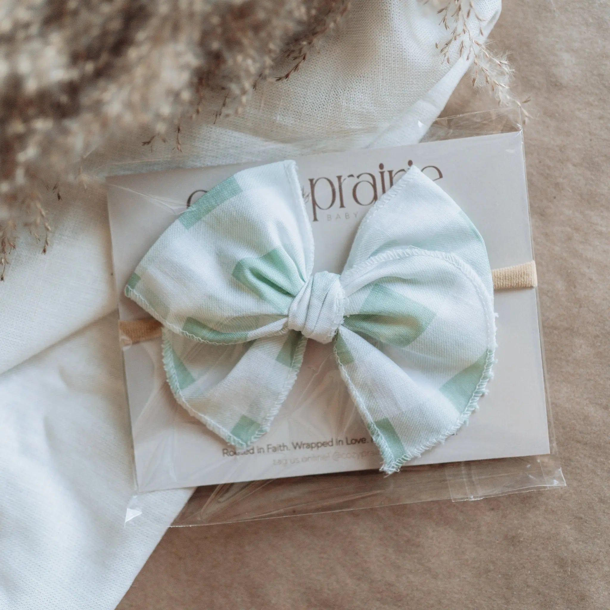 White bow hair accessory on a clear card with 'prairie' branding, placed on a textured surface.