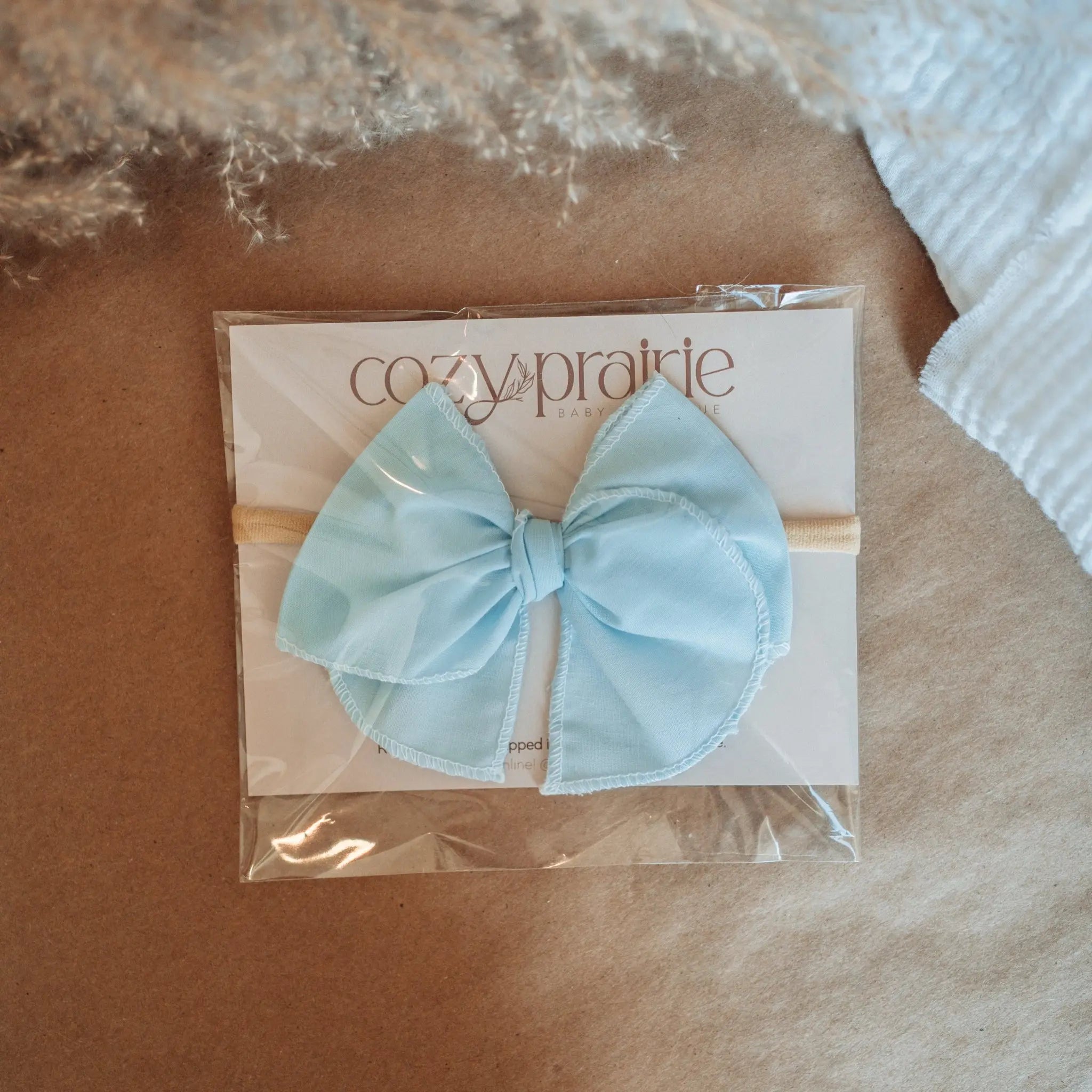 Sky Blue baby bow wrapped around a branded card against a brown paper background.