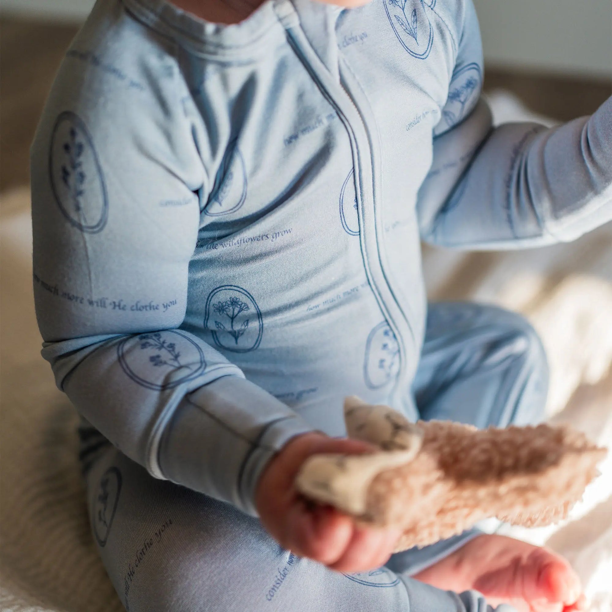 Baby in a blue onesie holding a textured toy