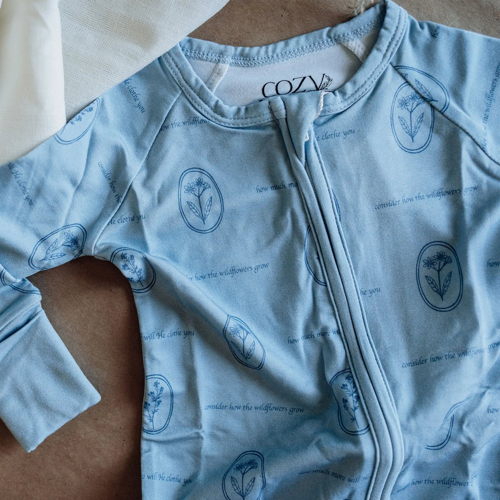 Light blue baby onesie with floral patterns and 'Cozy' branding on a wooden surface.