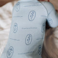 Baby wearing a light blue onesie with patterns and text